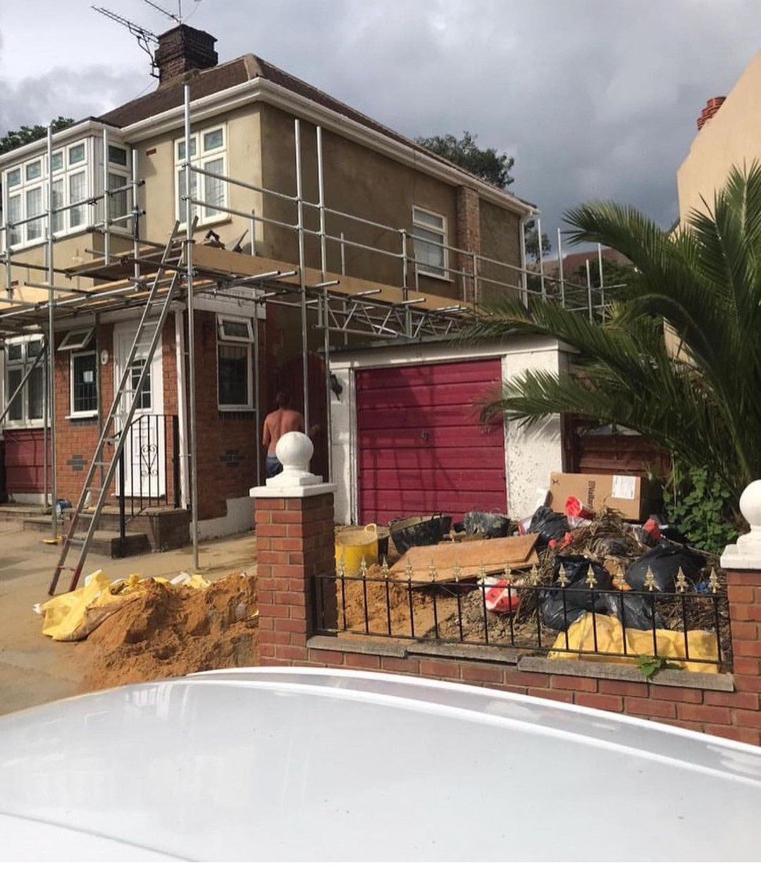 A semi-detached house under scaffolding with materials on the drive
